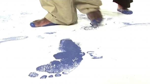 A blue footprint on a white floor with dancers feet covered in blue paint.