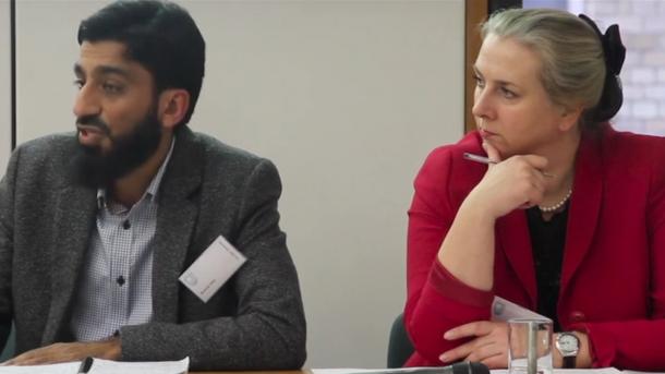 A man and woman sitting next to each other at a table looking off to the left.