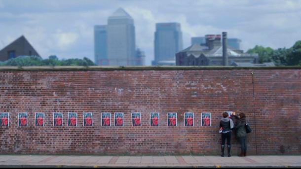 Two girls sticking up posters on a brick wall.
